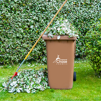 Brown bin in garden with pile of leaves